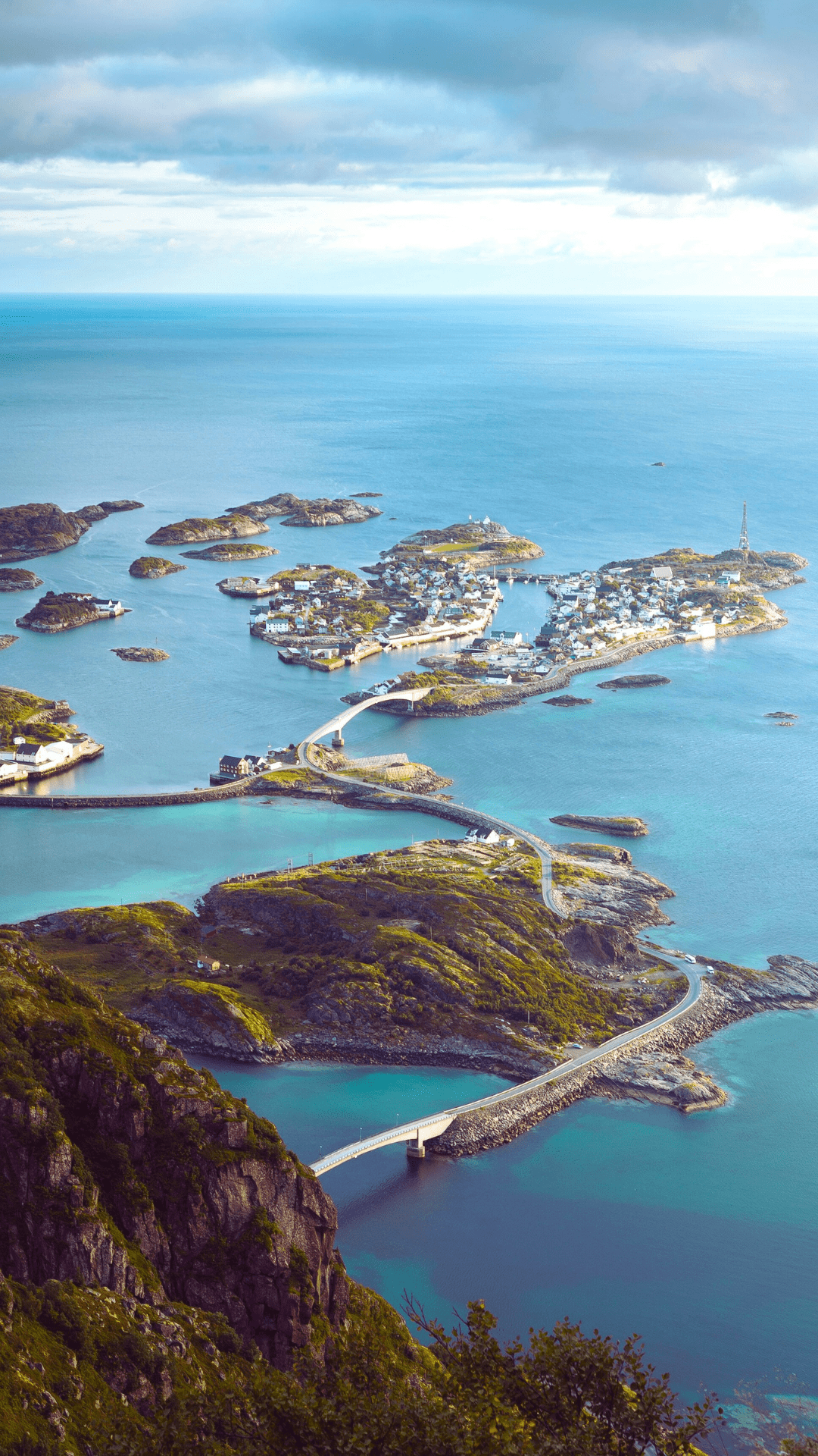 Aerial view of islands connected by bridges in a blue sea. Buildings dot the islands under a cloudy sky.