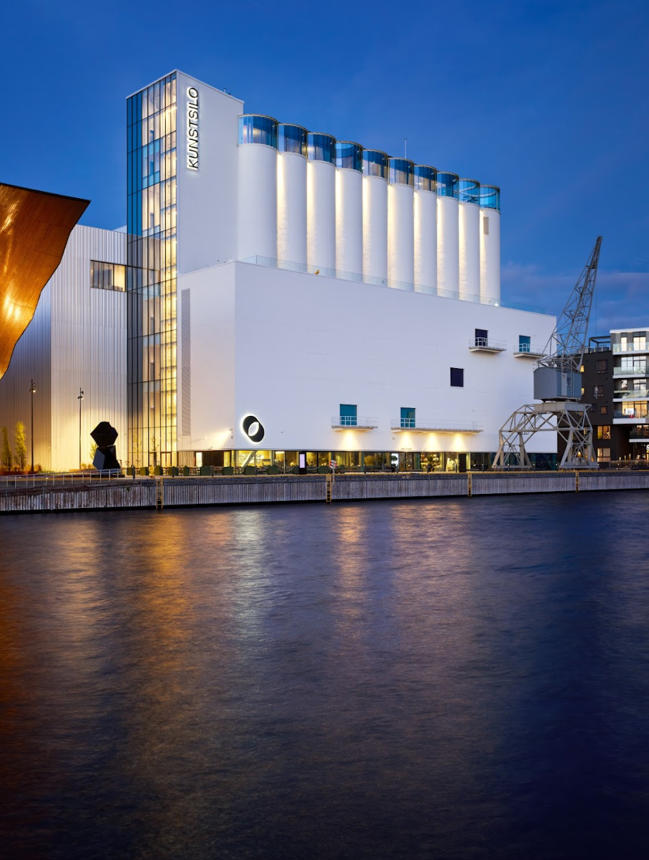 White hotel, a former grain silo, on waterfront at dusk.