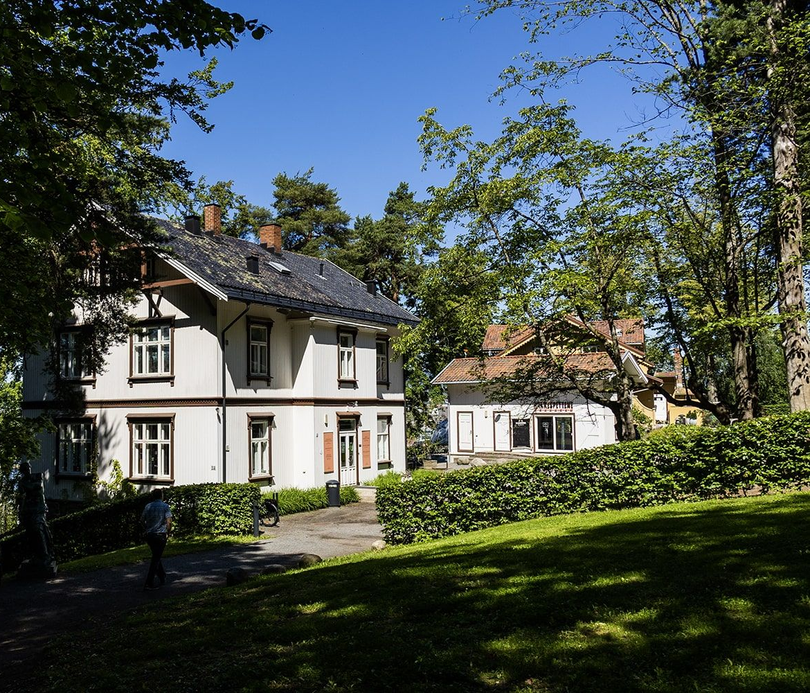 Two-story white house with dark roof and trim, nestled in a tree-lined yard with a smaller building in the background.
Photographer: Ekebergparken / Kristina Aurore Kvåle