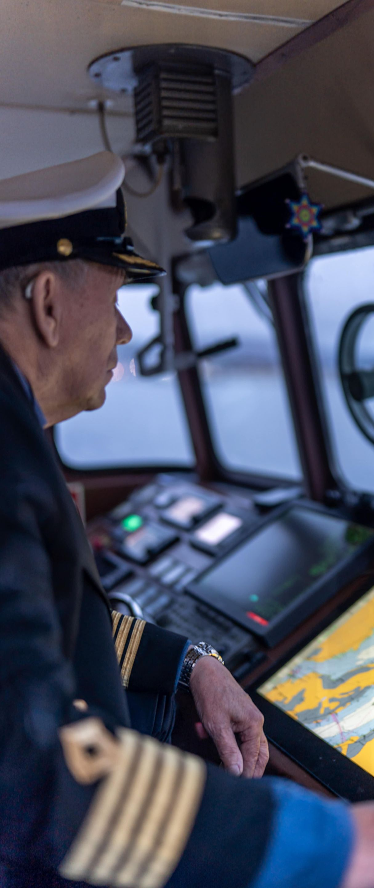 A person in a naval uniform at a ship's helm, looking at a navigation display.