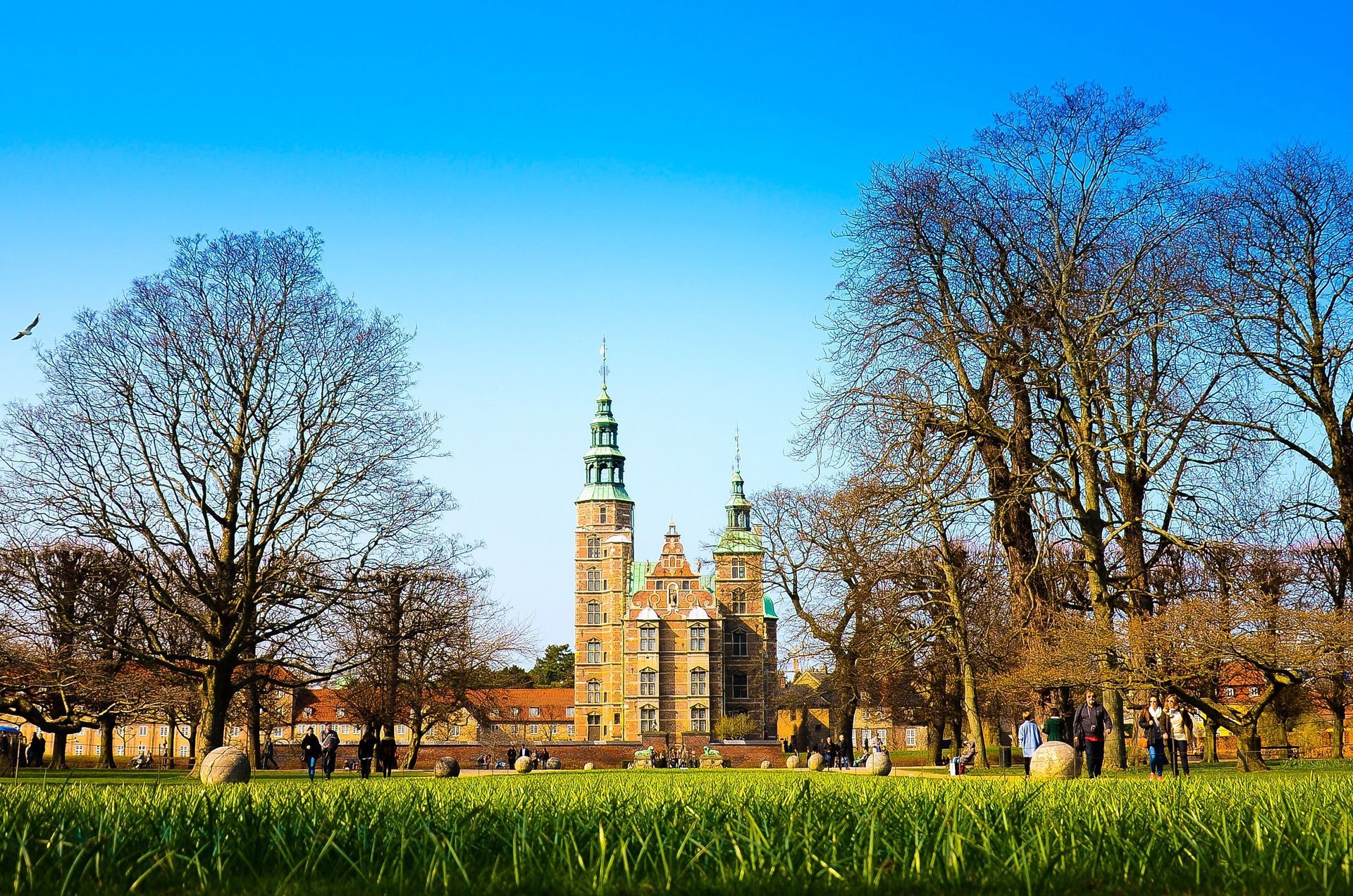 Historic castle with green towers behind a grassy park under a clear blue sky