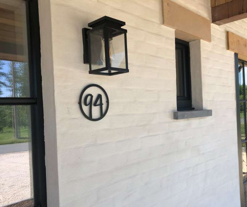 Een witte bakstenen muur met een zwarte lantaarn en het nummer 94 erop.