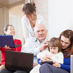 A family sits together with laptops and a handheld device, interacting in a brightly lit indoor space.