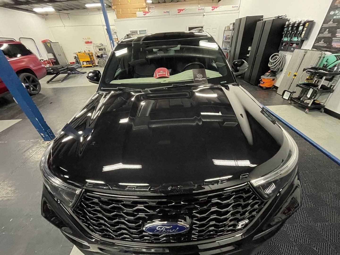Black Ford SUV in a garage, viewed from the front, with hood open and a pink item on the dashboard