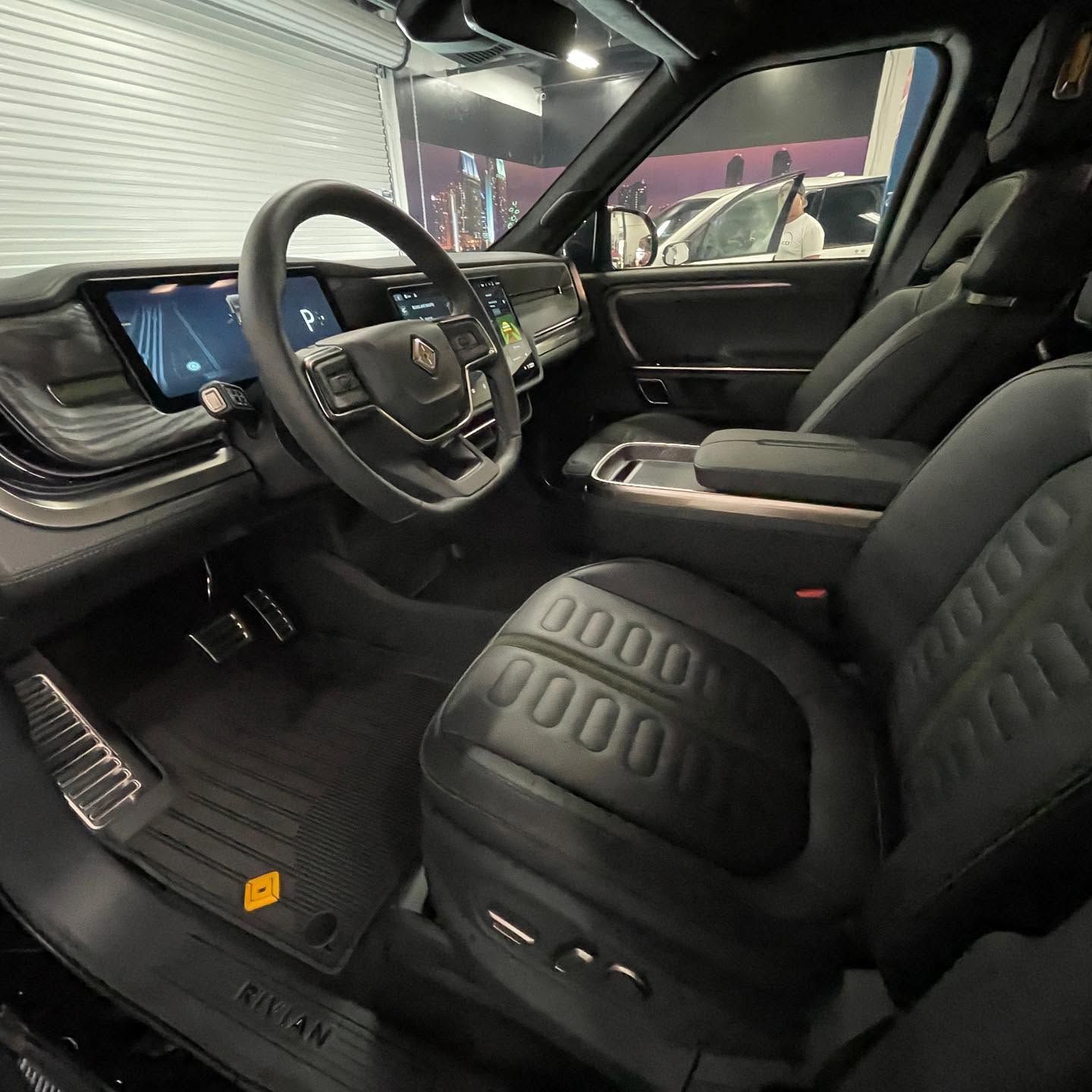 Modern car interior with black seats, dashboard display, and steering wheel seen from the open door
