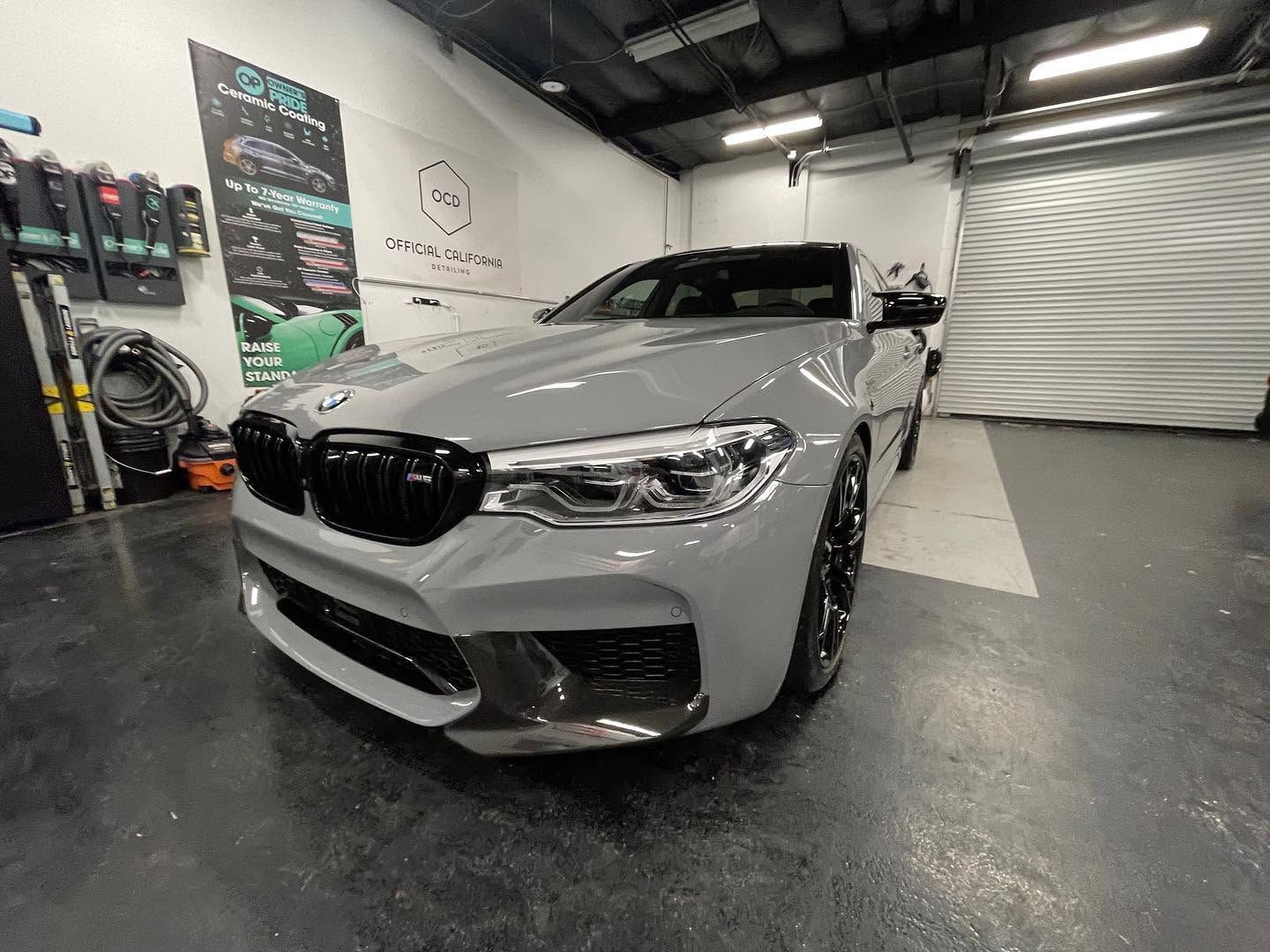 Silver BMW sedan in a garage, angled front view with black grille and polished floor reflections