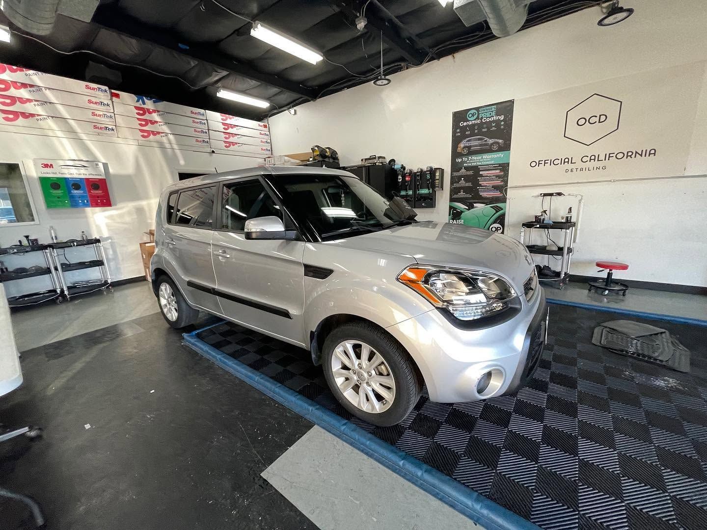 Silver SUV in a showroom or service bay, parked on a blue platform under bright lights.