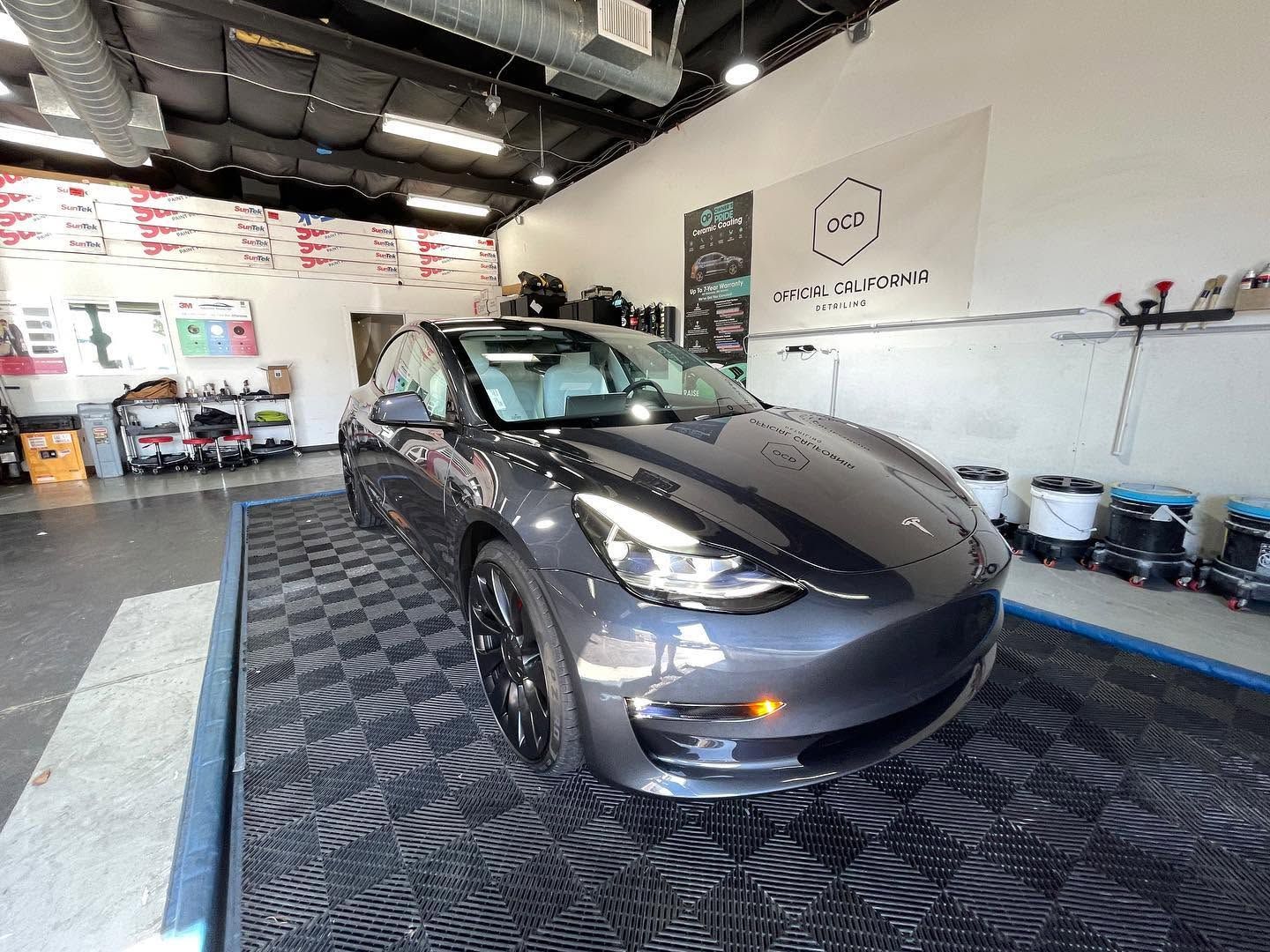 Gray sedan in a car detailing garage, parked on a patterned floor under bright lights.