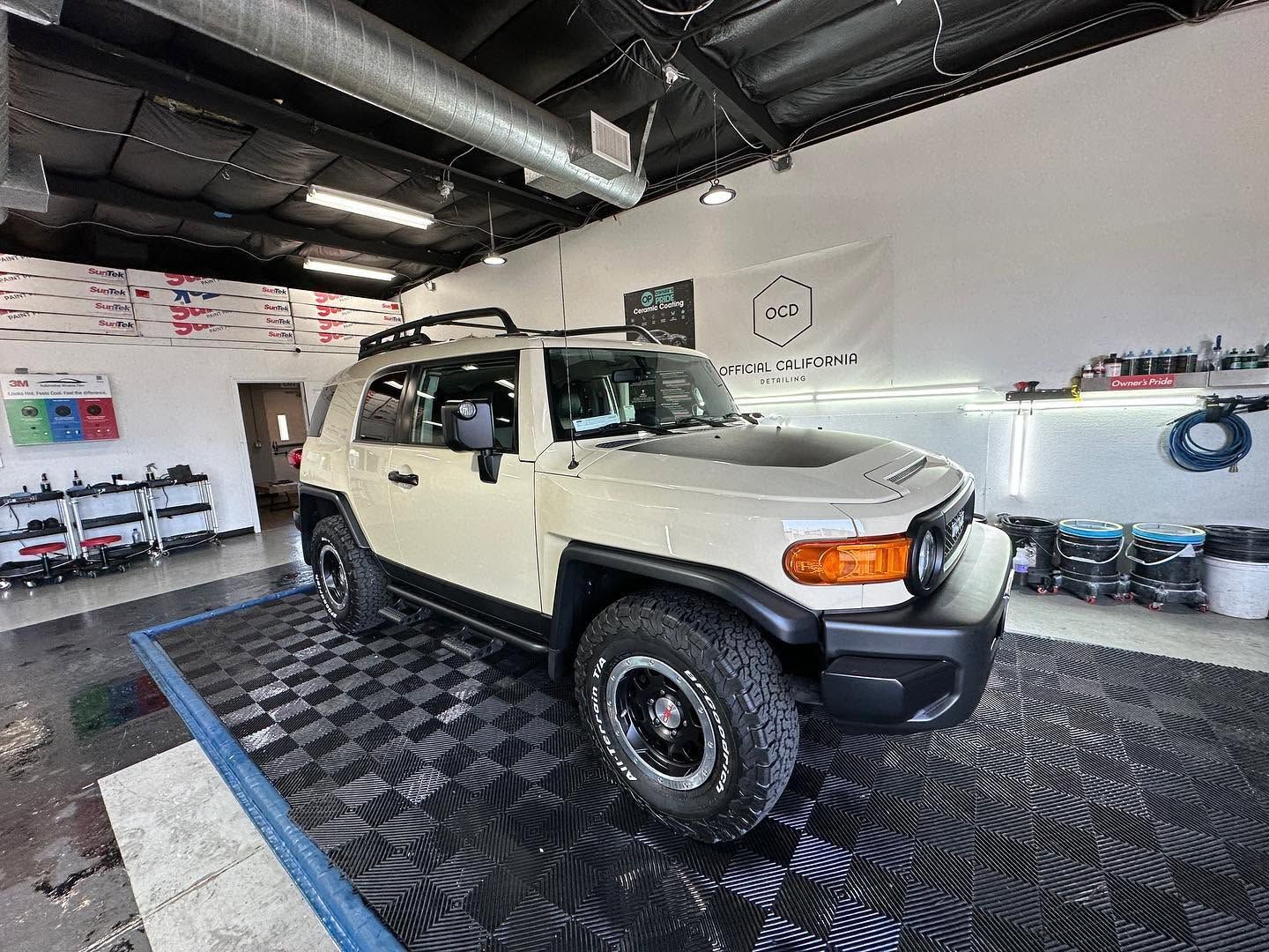 Cream Toyota FJ Cruiser in a bright auto shop with black checkered floor and white walls