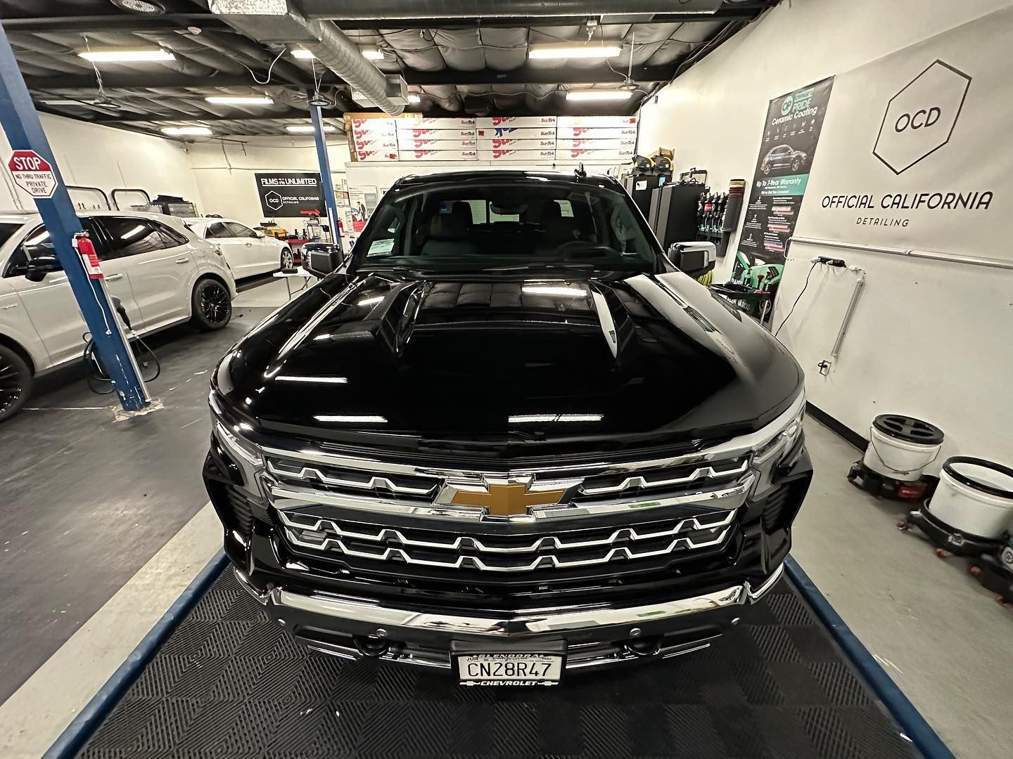 Black Chevrolet SUV in an auto shop bay, front view under bright lights.