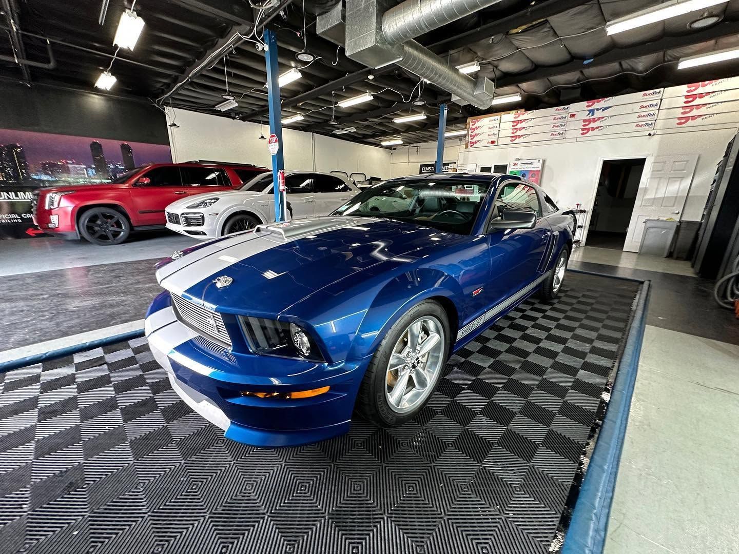 Blue Ford Mustang convertible on a showroom floor with a red car in the background.