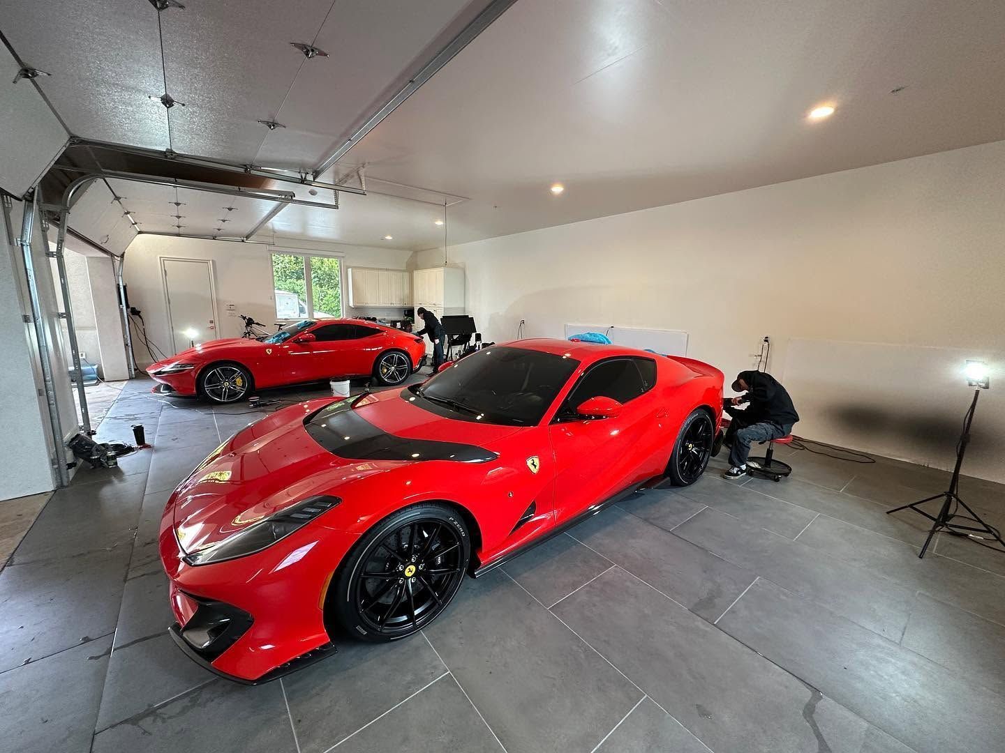 Two red sports cars in a bright garage, one in the foreground and one parked near the back.