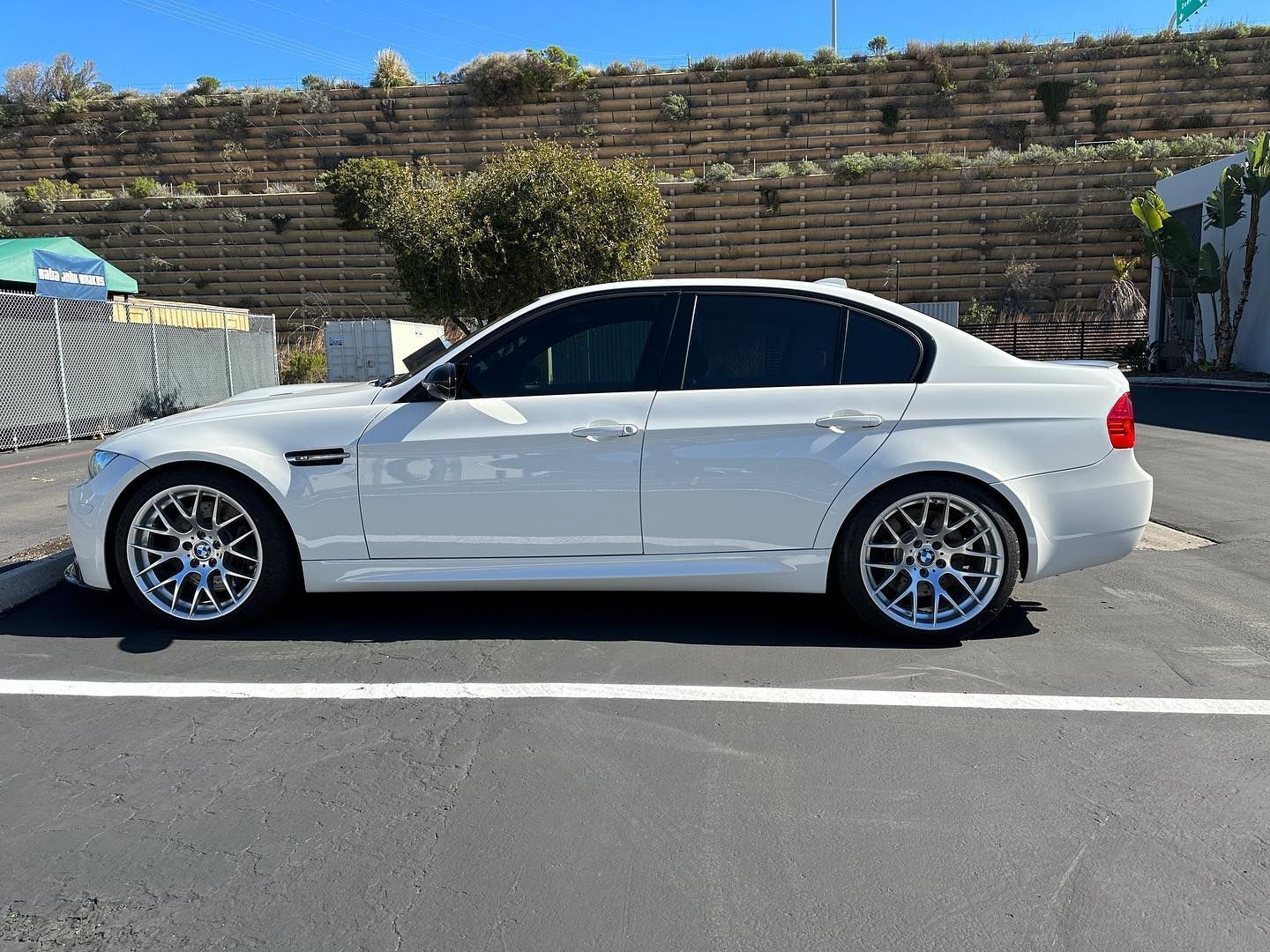 White sedan parked on a street beside a stone wall, with tinted windows and silver rims.