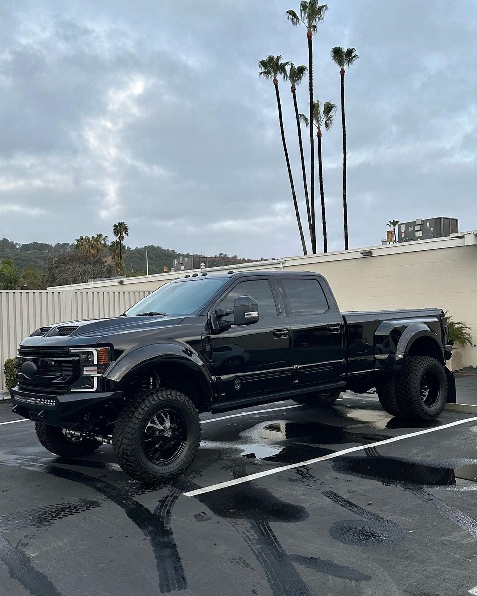 Black lifted pickup truck parked in a wet lot with palm trees and cloudy sky in the background
