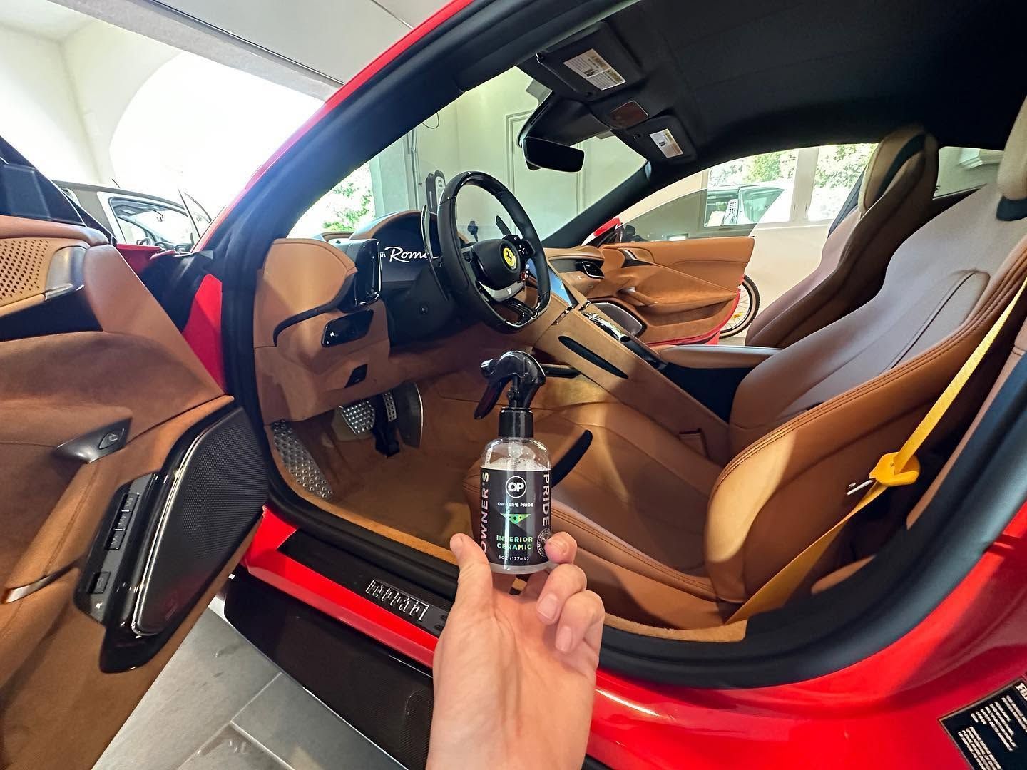 Hand holding a car key fob beside a red sports car with tan leather interior and open door