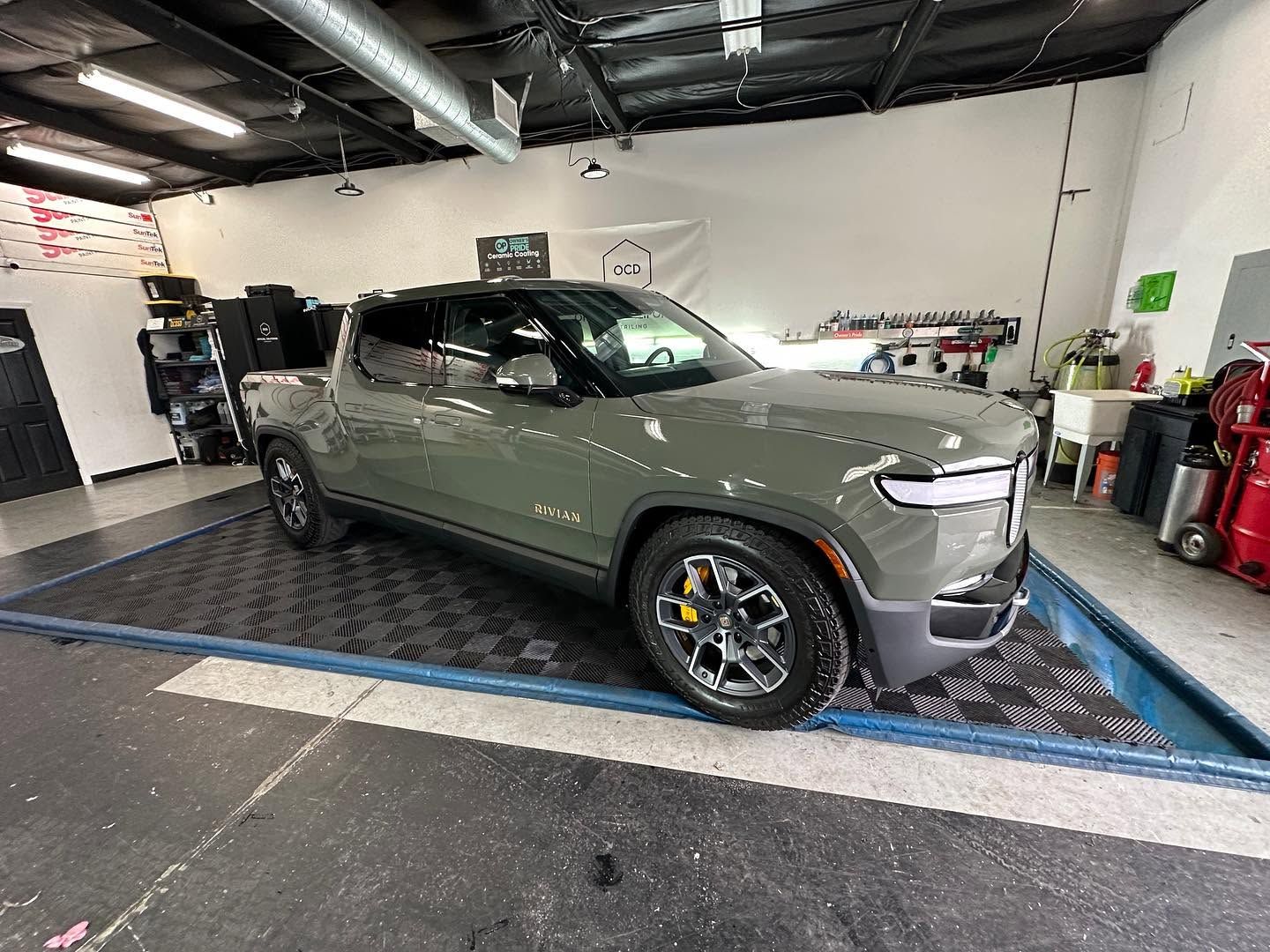 Green SUV in an auto garage, parked on a lift platform with tools and equipment nearby