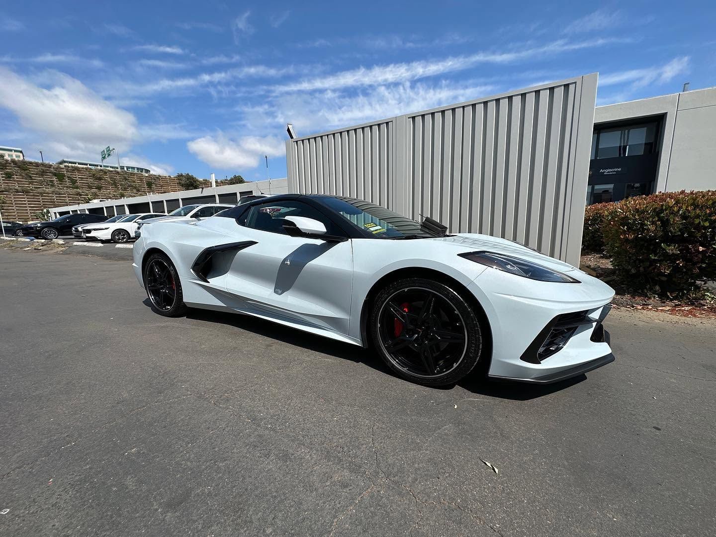 White sports car parked outdoors beside a building under a blue sky.