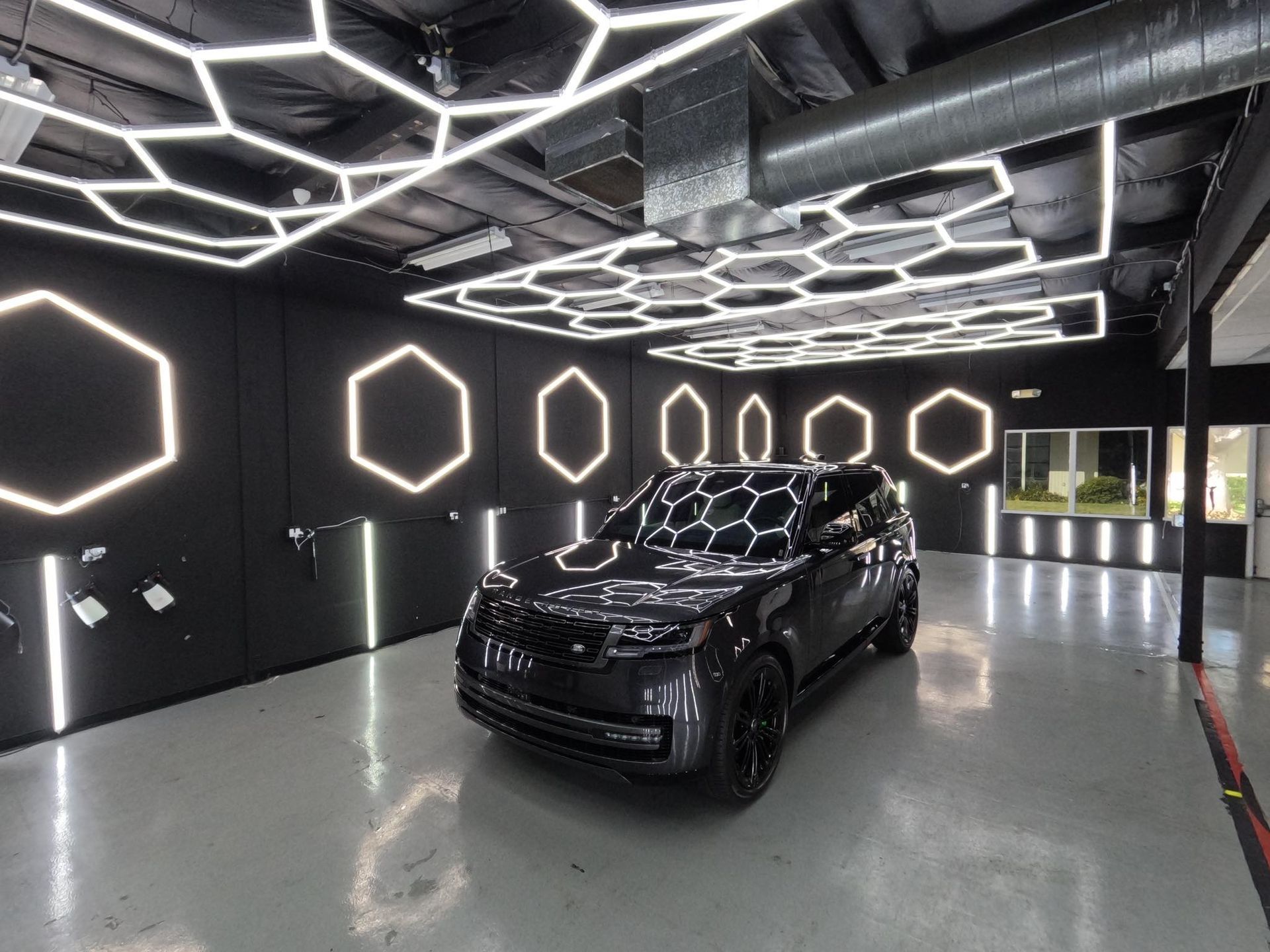 Black SUV in a futuristic garage with glowing hexagon lights on the walls and ceiling