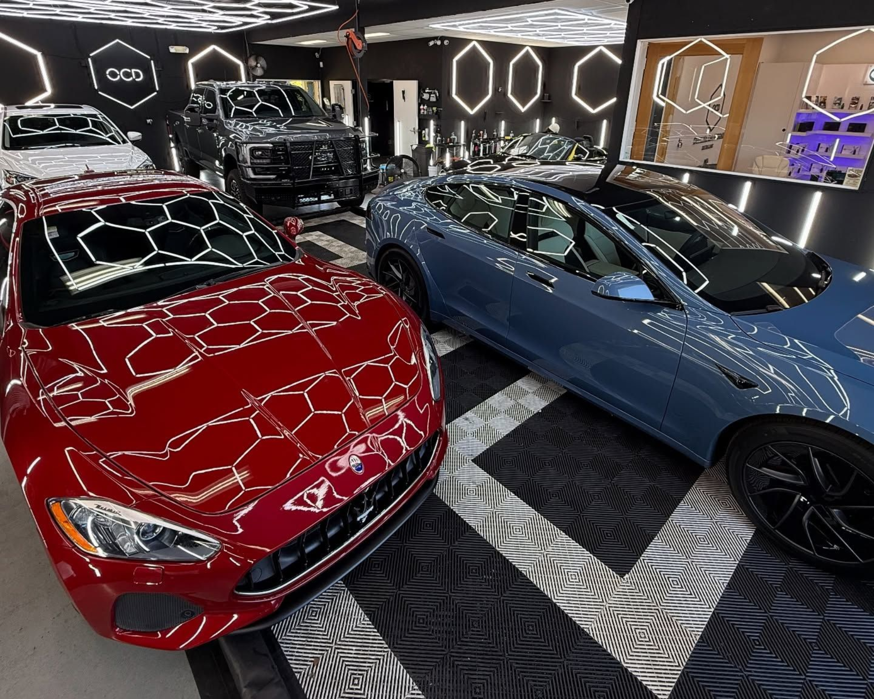 Red and blue luxury cars in a showroom with geometric black-and-white flooring