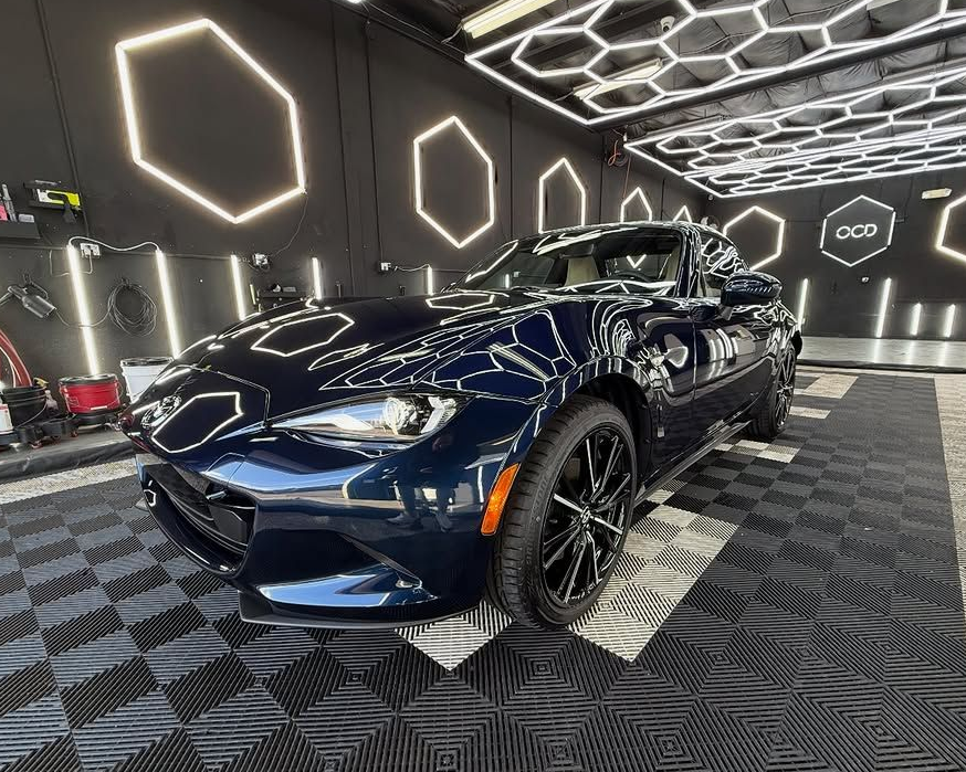 Dark blue sports car in a modern showroom with hexagonal wall lights and black checkered flooring