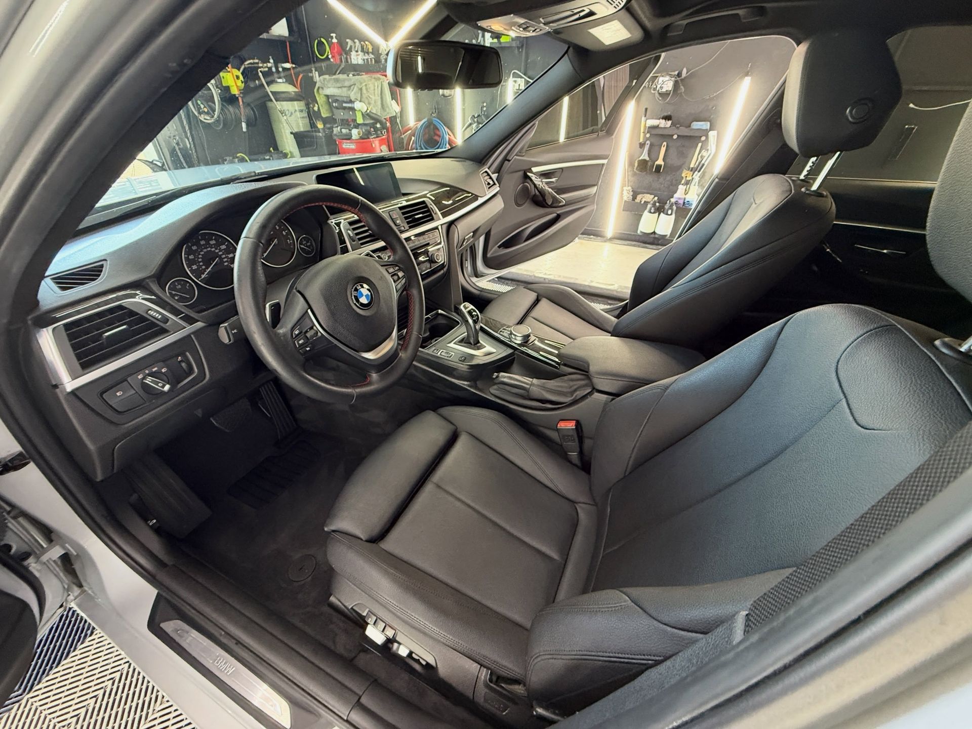 Car interior with black leather seats, dashboard, steering wheel, and center console viewed from the open door