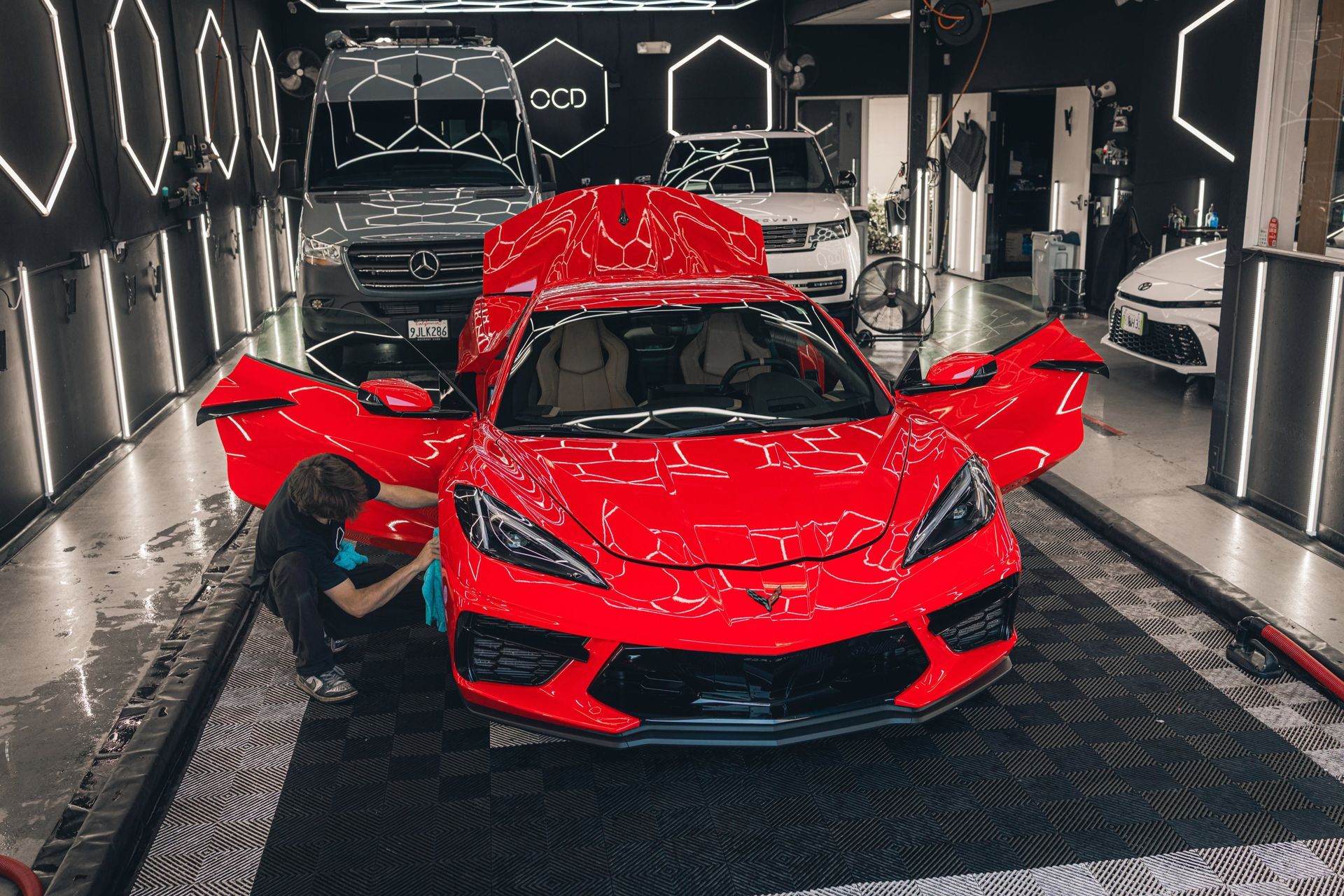 Red sports car in a detailing bay with doors and hood open, glossy reflections on the floor