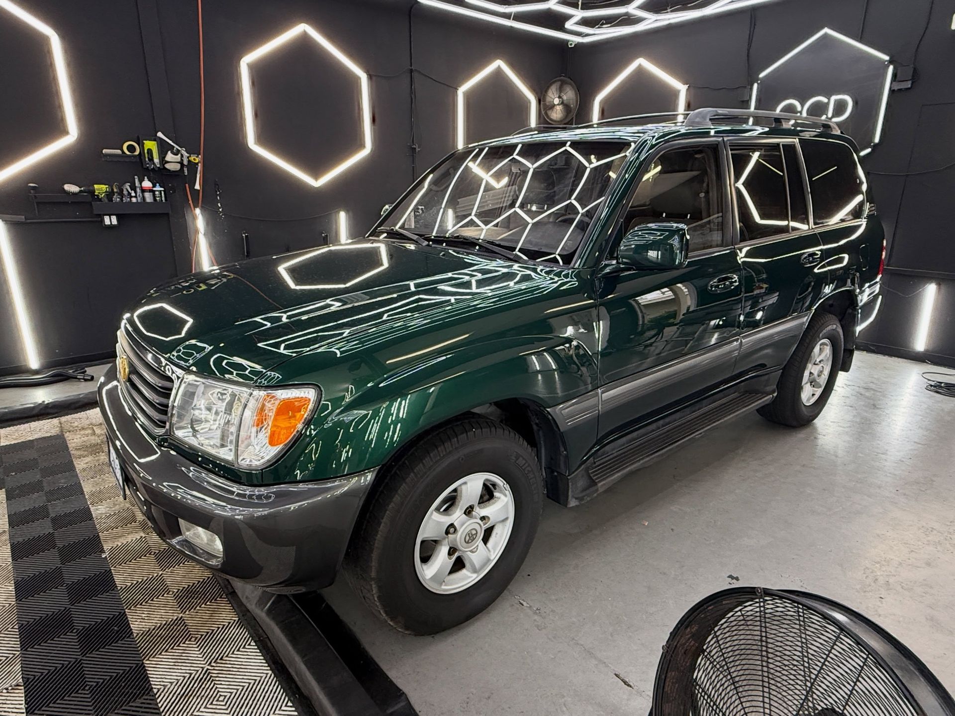 Dark green SUV on display indoors with geometric neon wall lights behind it