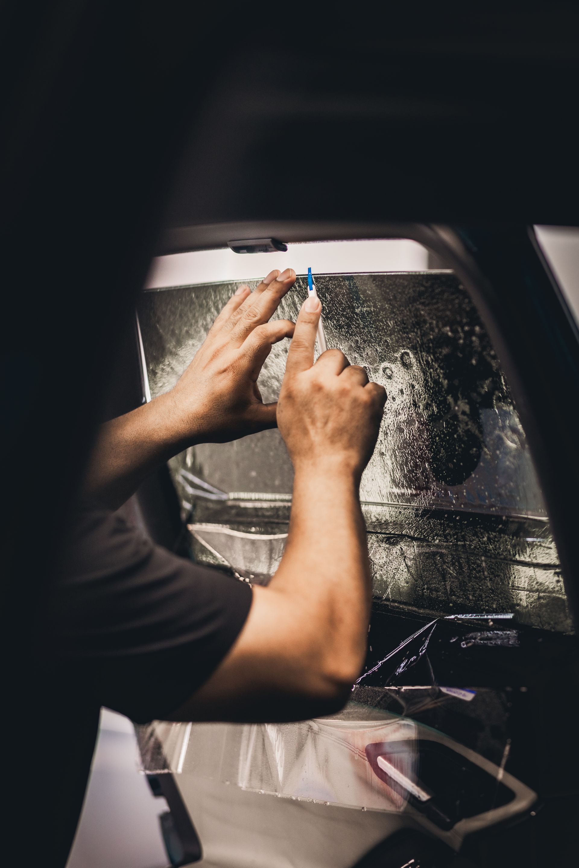Hands cleaning a car windshield with a cloth from inside the vehicle.