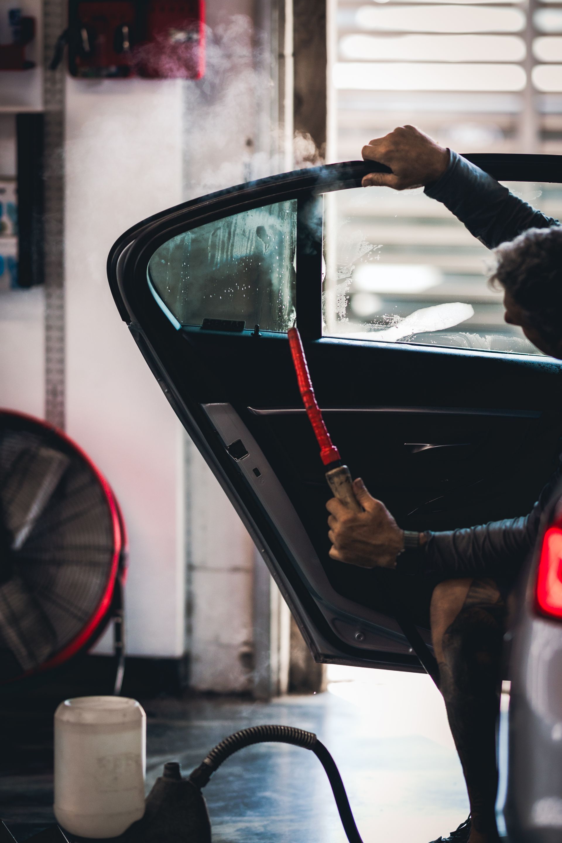 Person cleaning a car door with a steam hose in a garage