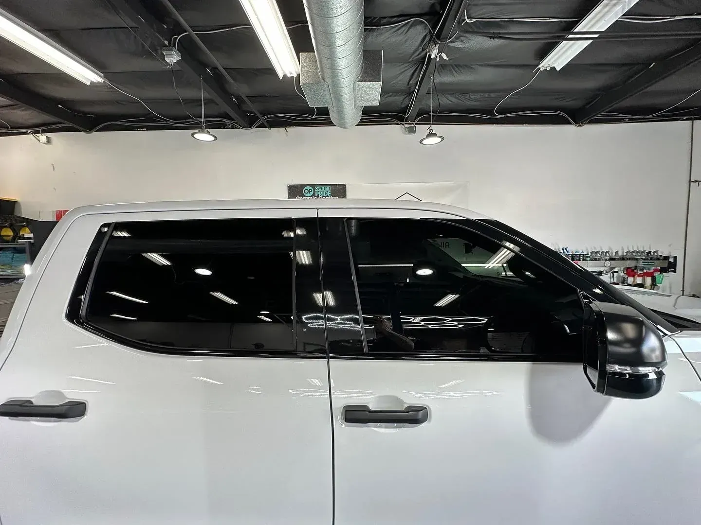 White SUV parked indoors in a garage, side view with tinted windows under bright overhead lights