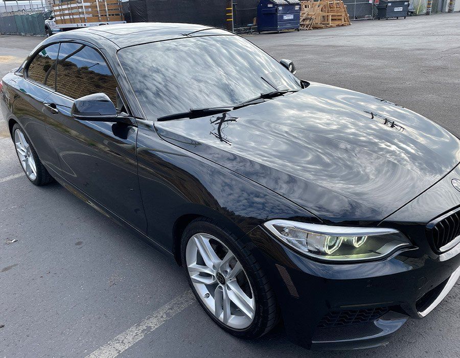 Black sedan parked on a street in an industrial lot, front three-quarter view.