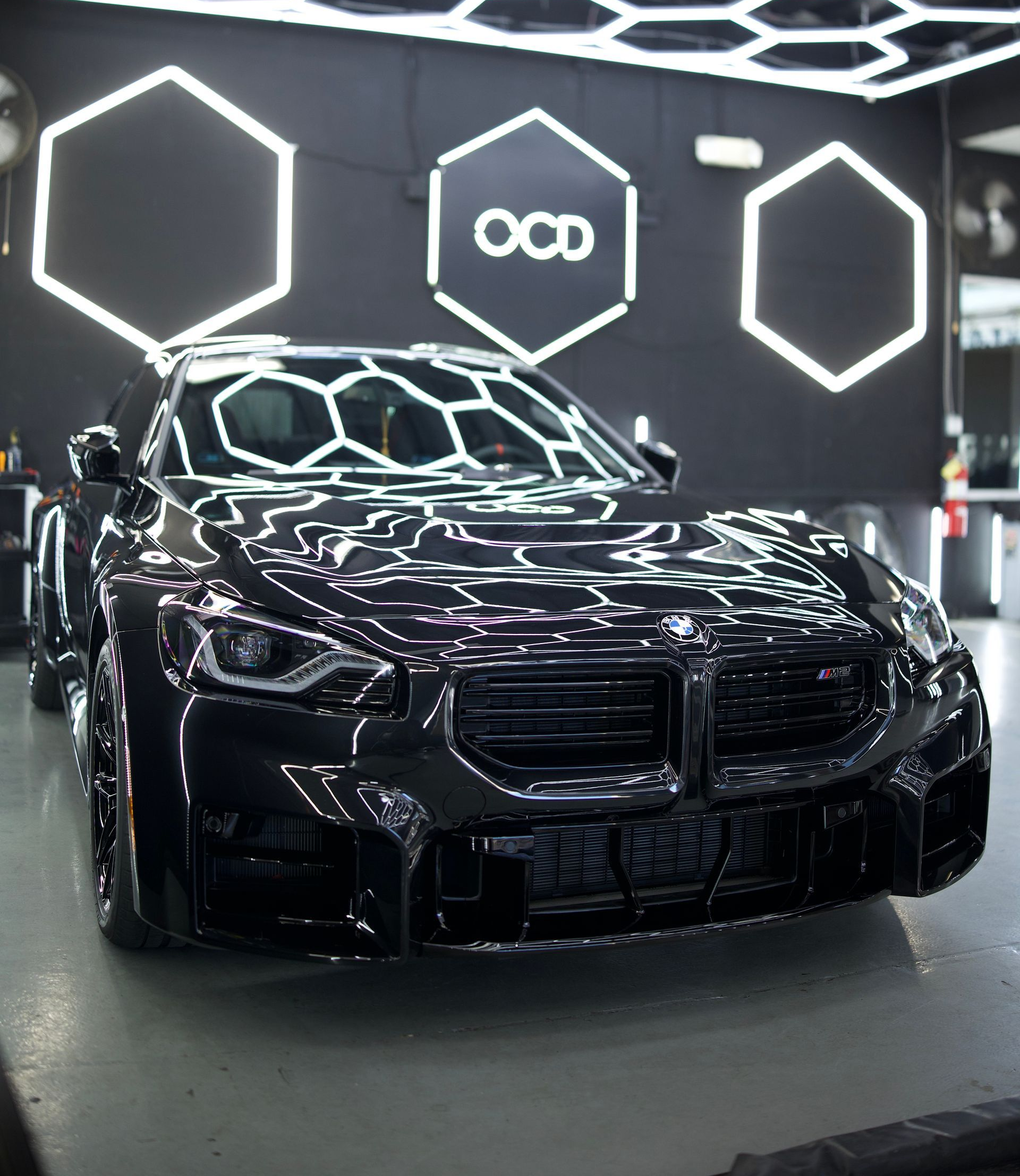 Black luxury sports car in a showroom under bright geometric hexagon lights.