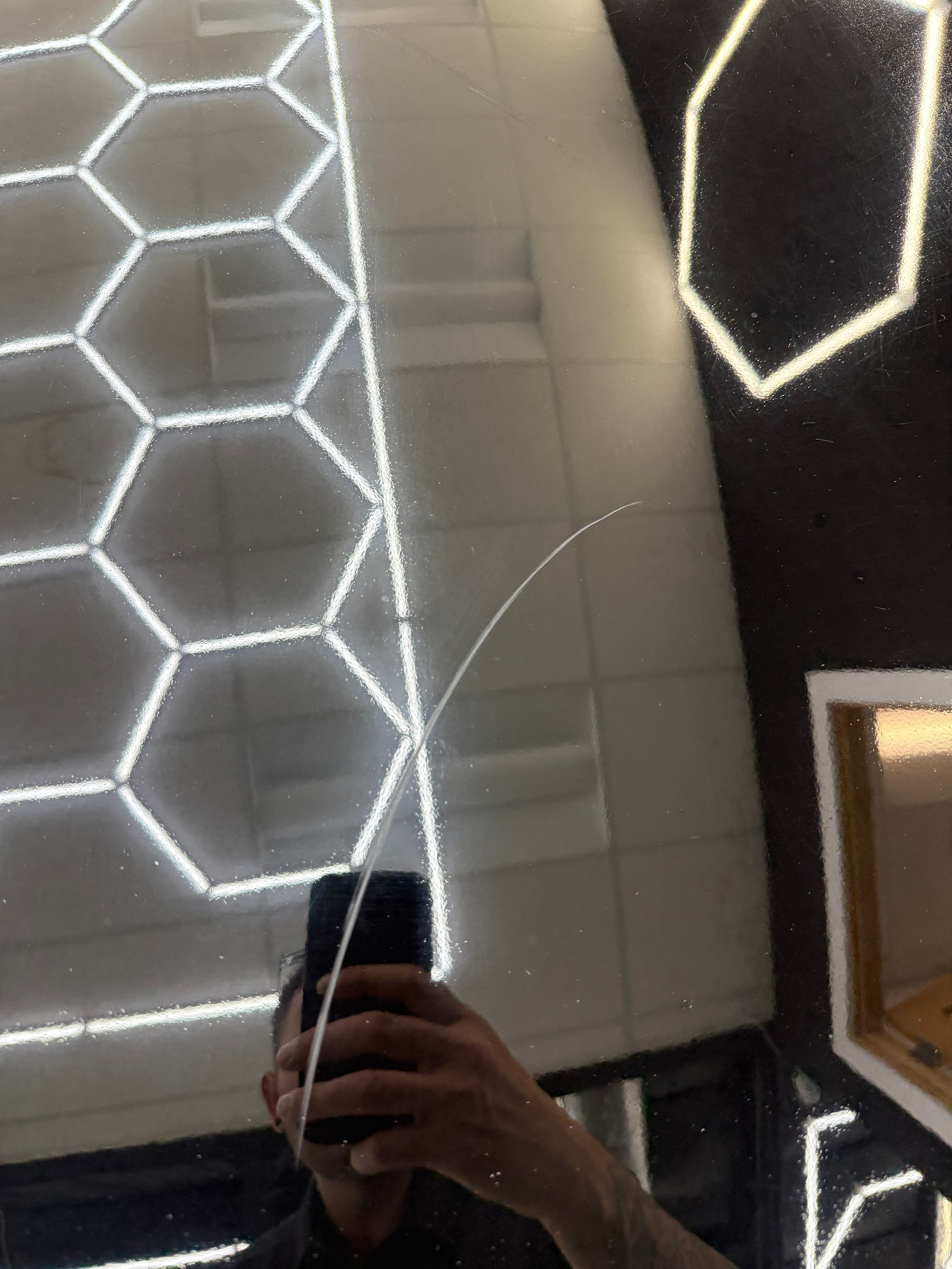 Person holding a phone in a mirror, reflecting geometric white LED lights and a tiled ceiling.