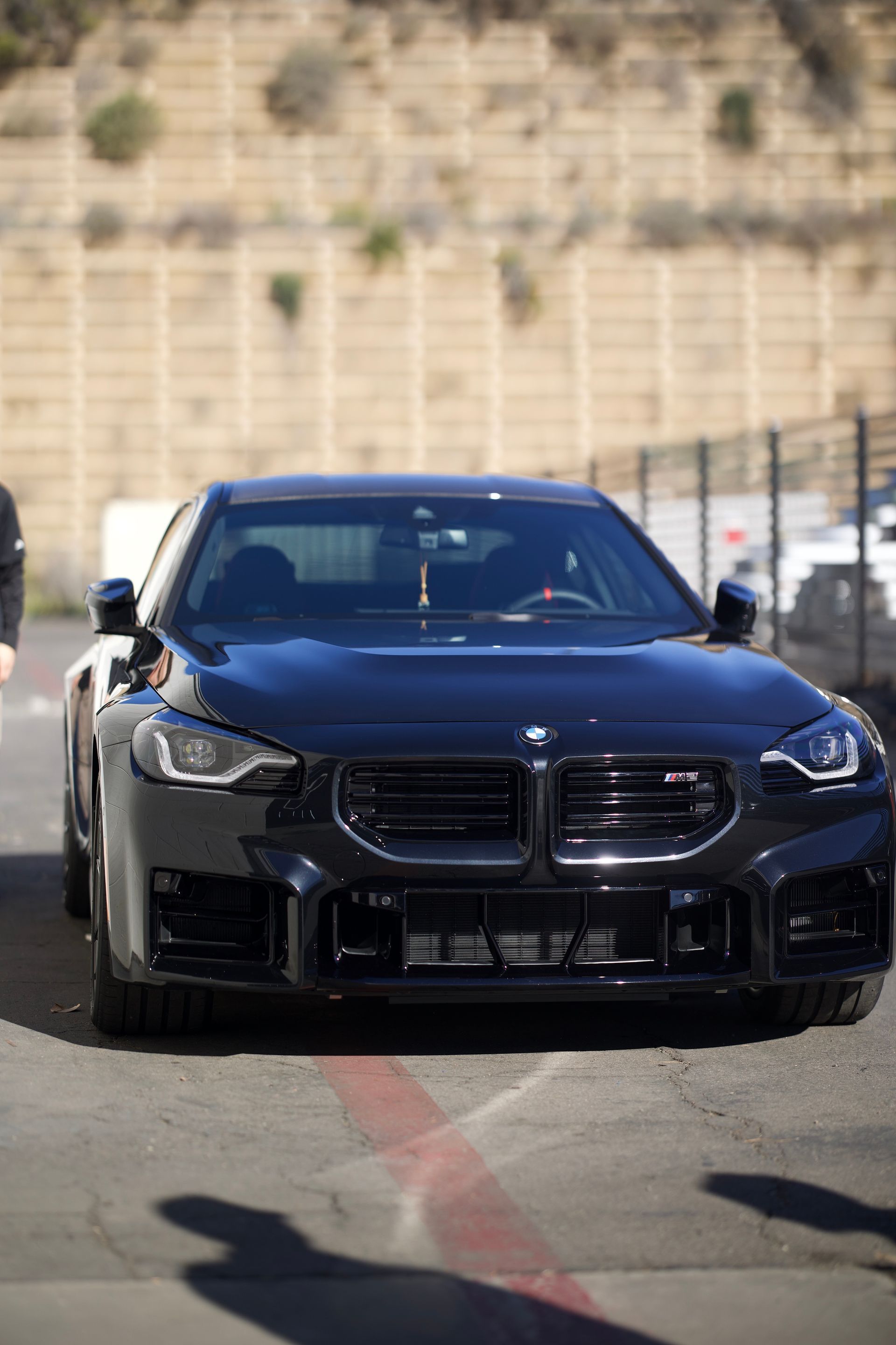 Black sports sedan driving on a track, front view with a blurred wall background