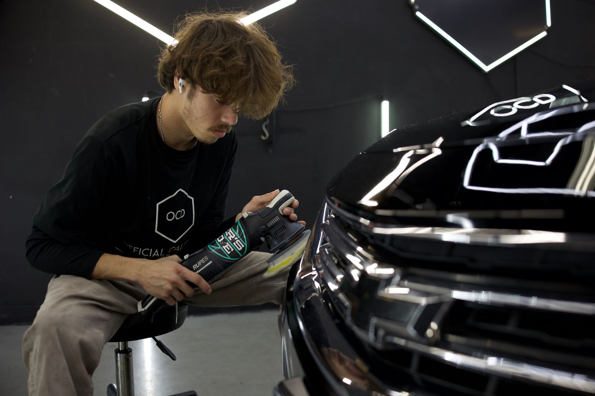 Detailing a black car in a modern garage with neon lights, using a spray bottle and cloth
