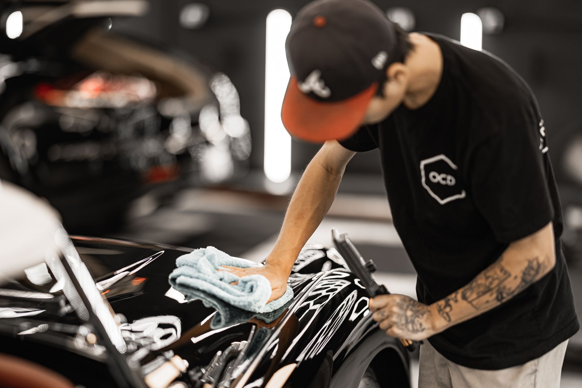 Person cleaning a black car with a microfiber cloth in a garage