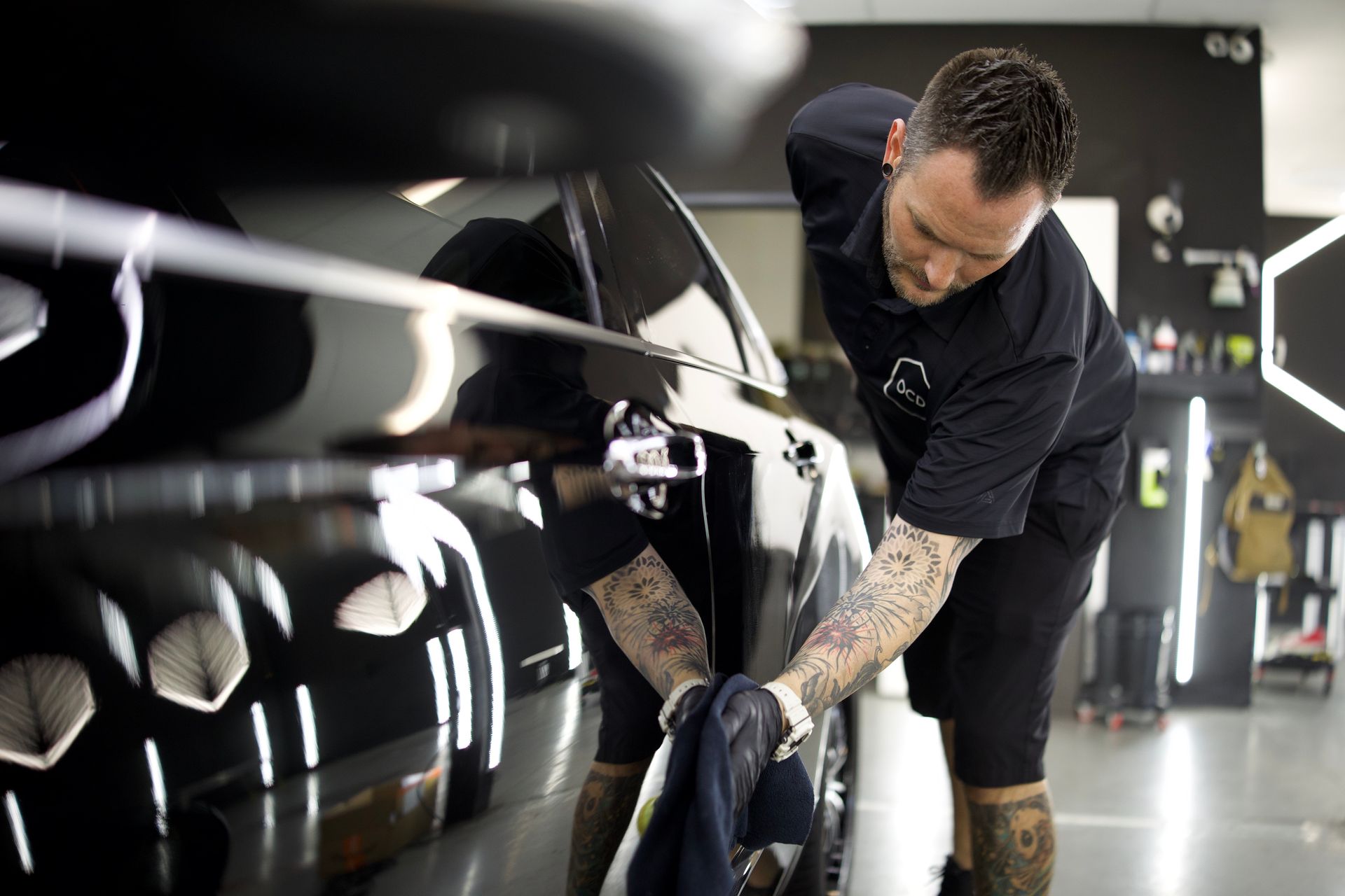 Detailing a glossy black car in a workshop, a person polishing the side panel by hand