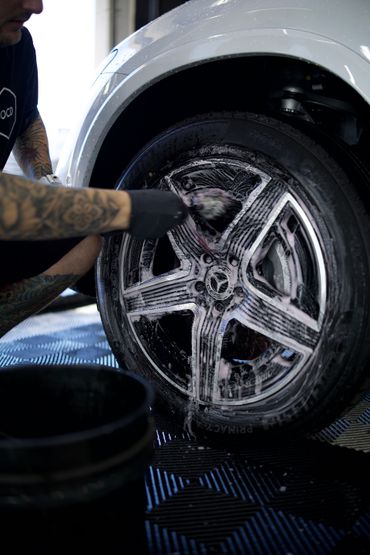 Person washing a white car wheel with soapy foam in a car wash.
