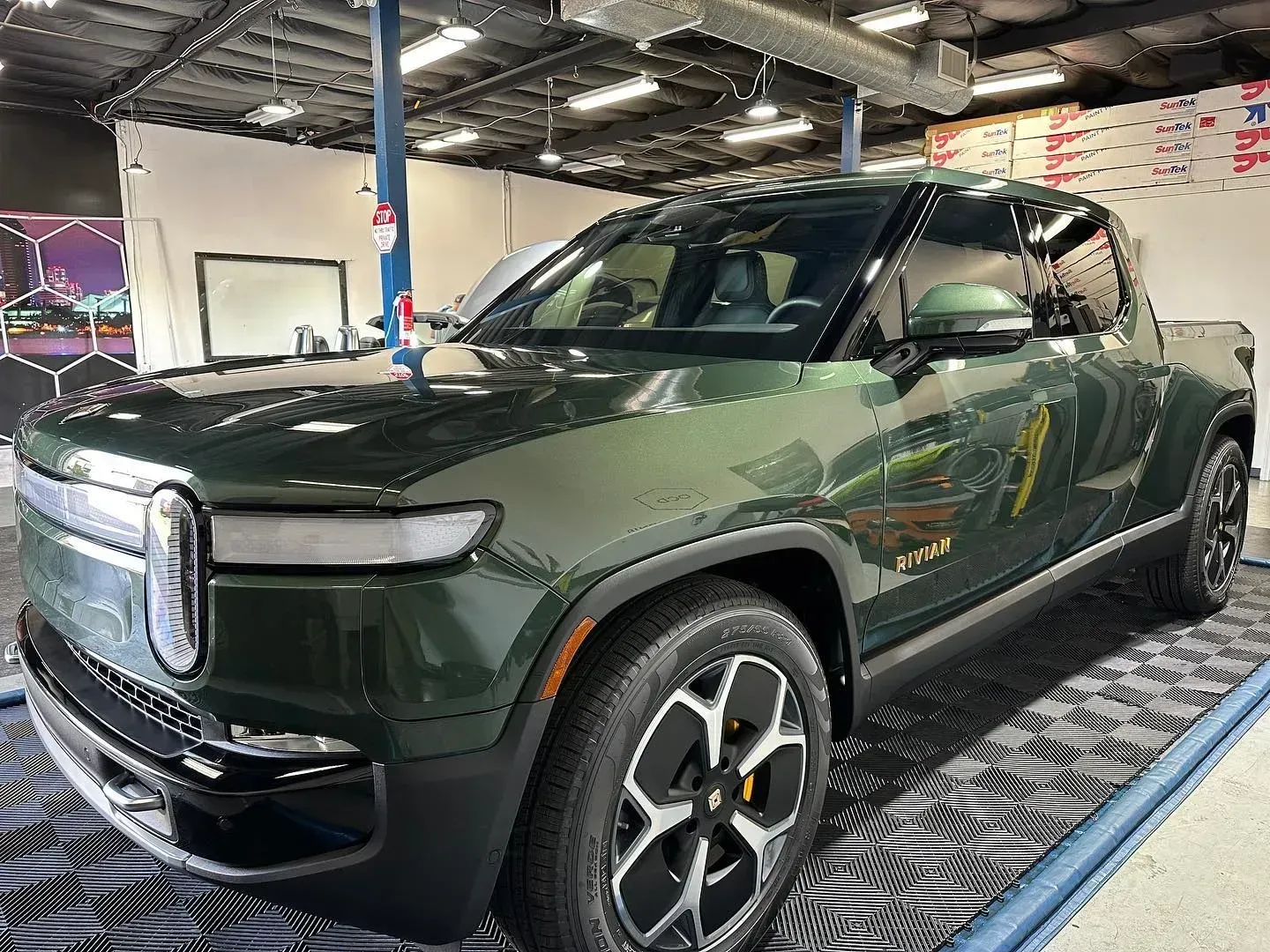 Dark green pickup truck in an indoor workshop, front three-quarter view on a lift.