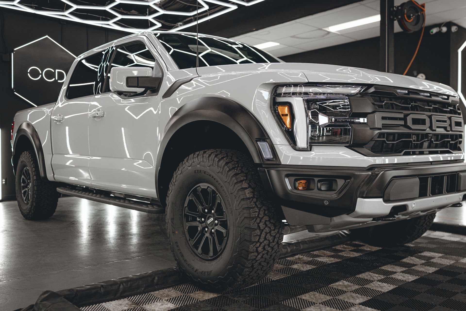 White off-road pickup truck in a showroom, with black wheels and rugged tires