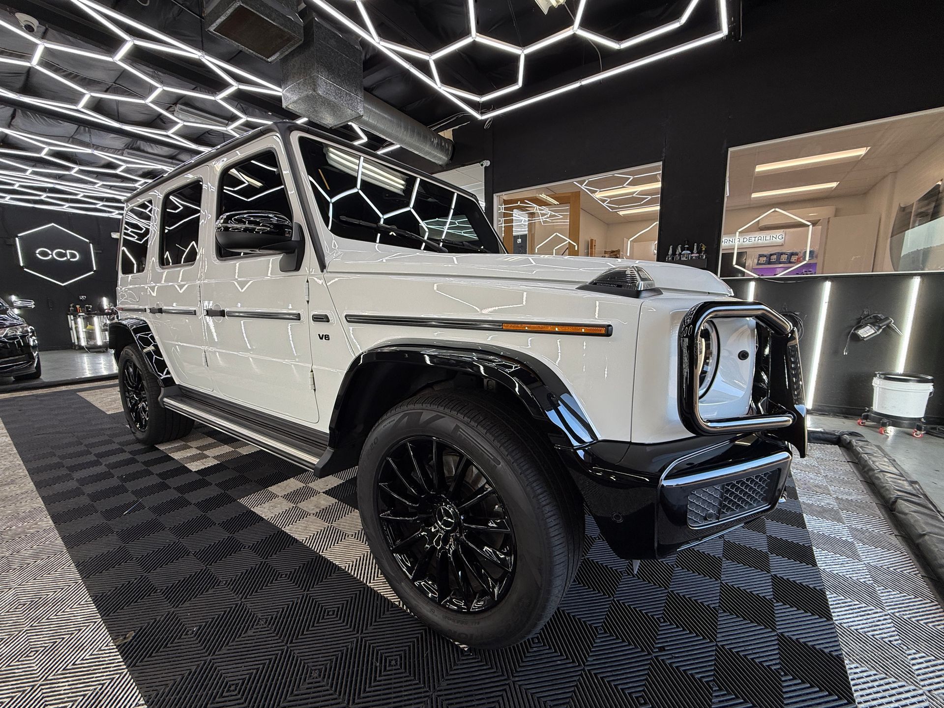 White Mercedes G-Class SUV on display in a showroom with geometric ceiling lights