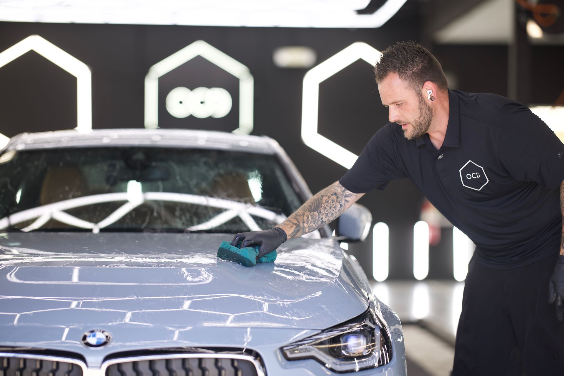 Detailer polishing a silver BMW in a car wash or studio setting