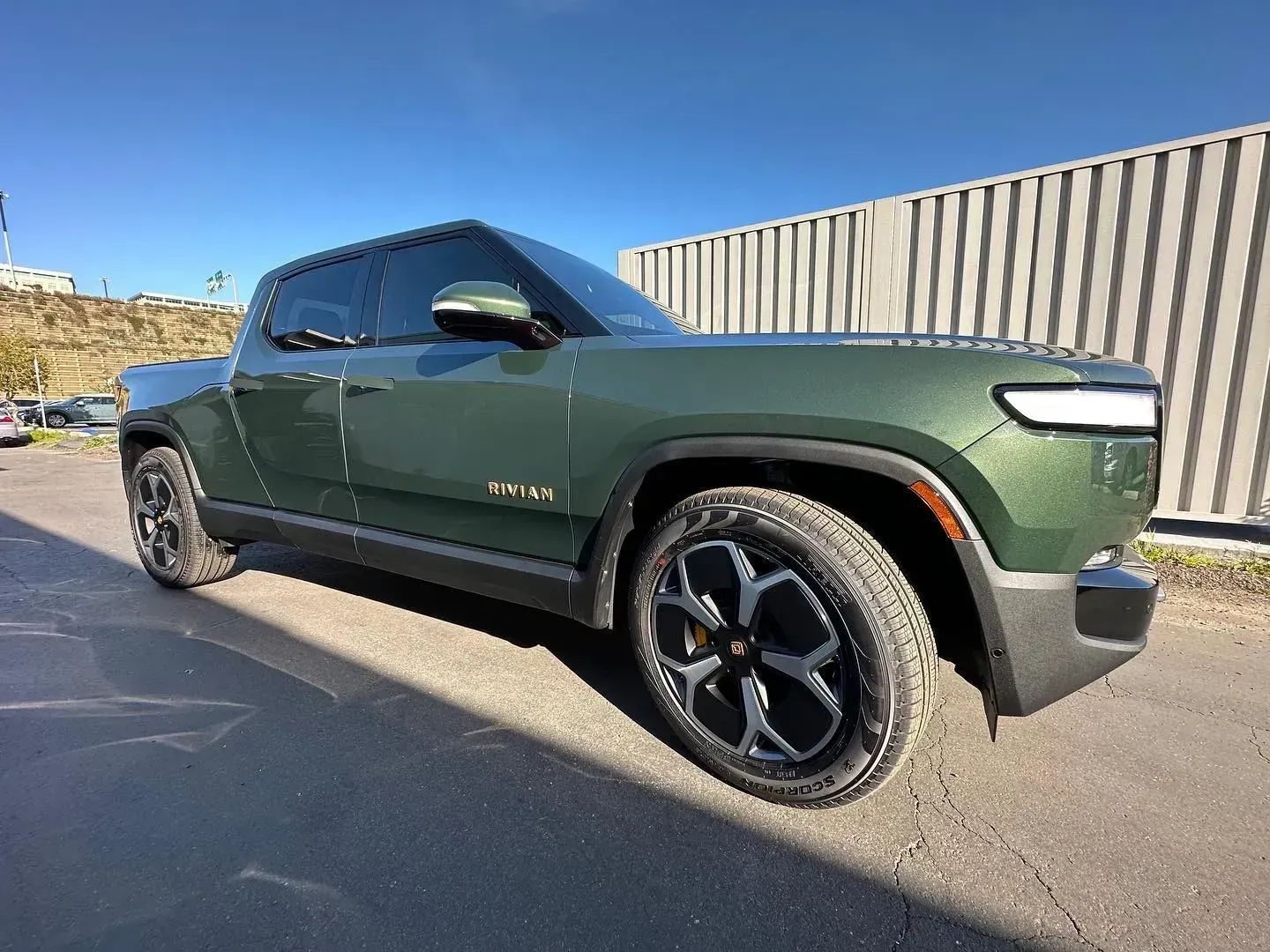 Green pickup truck parked on a sunny street beside a wooden fence