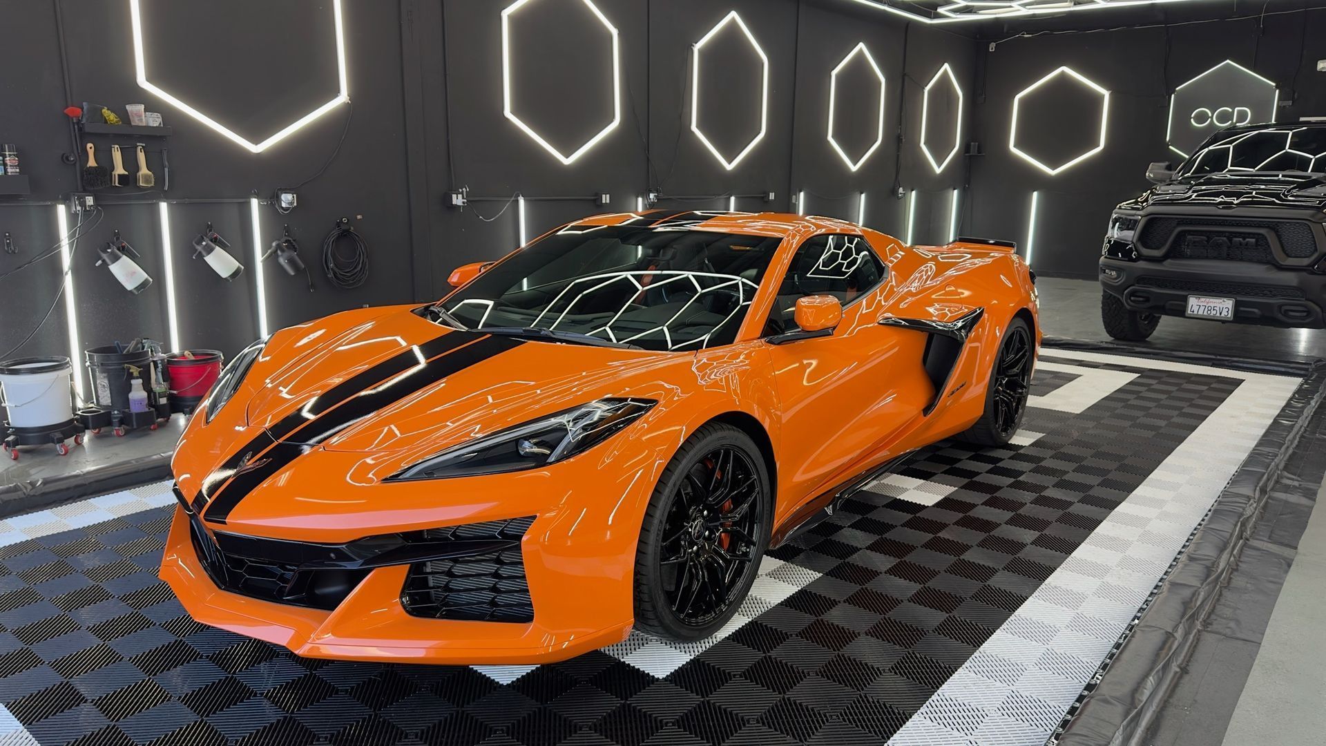 Orange sports car displayed in a showroom with geometric wall lights and a black SUV in the background