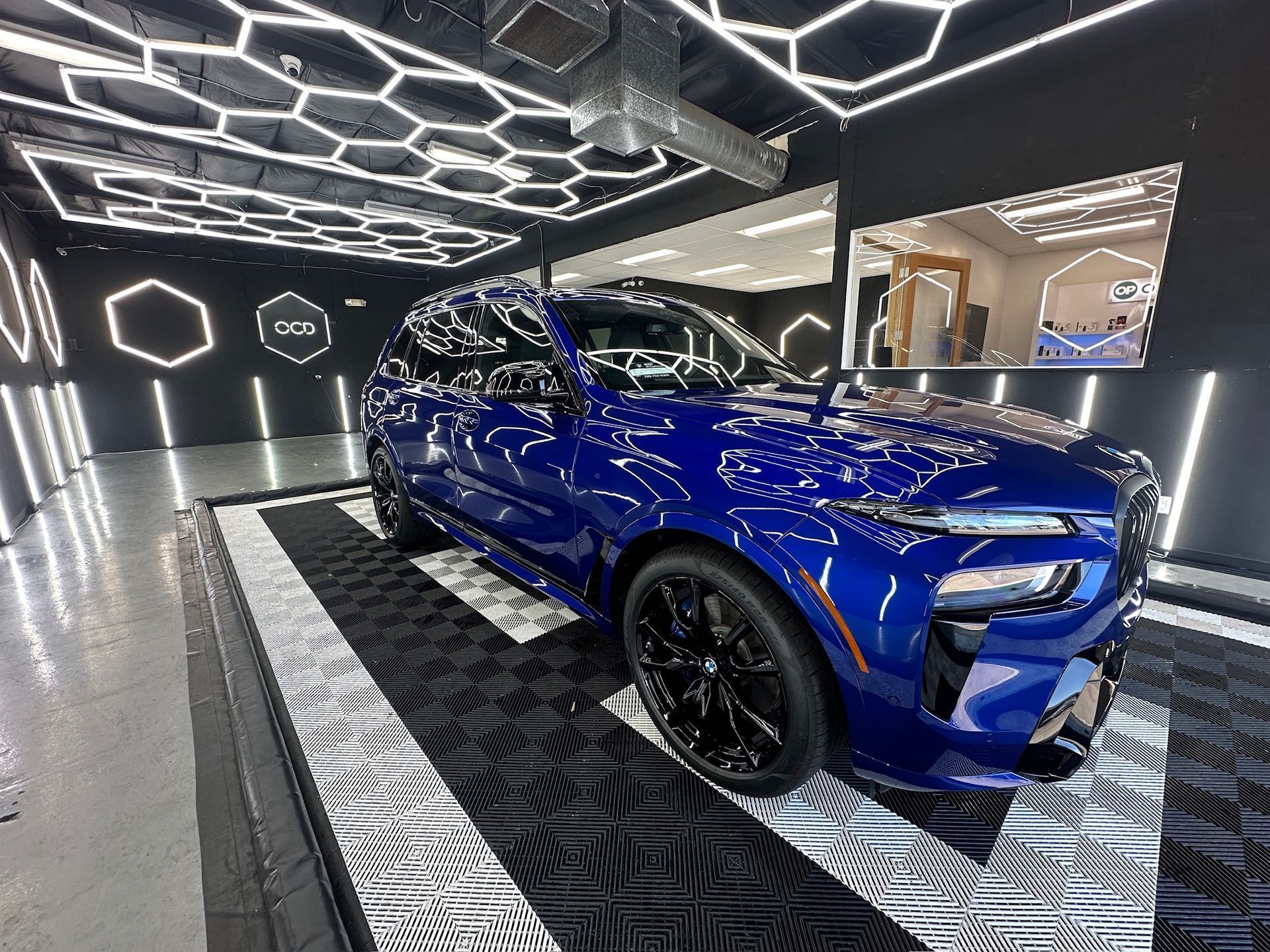 Blue sports car in a futuristic showroom with geometric LED ceiling lights and patterned floor.