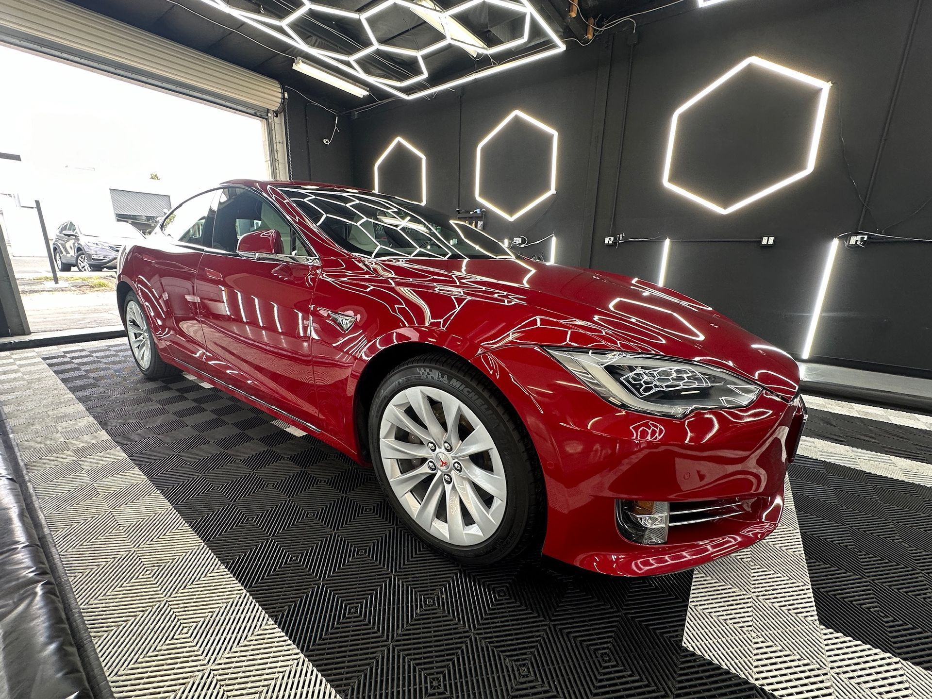 Red sports coupe in a modern showroom with hexagonal wall lights and patterned floor.