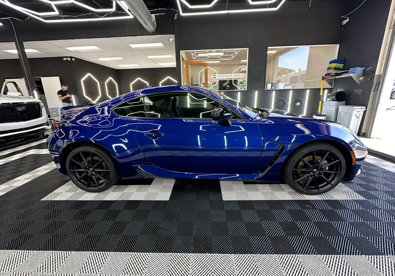 Blue sports coupe displayed indoors in a showroom, side view on a checkered floor