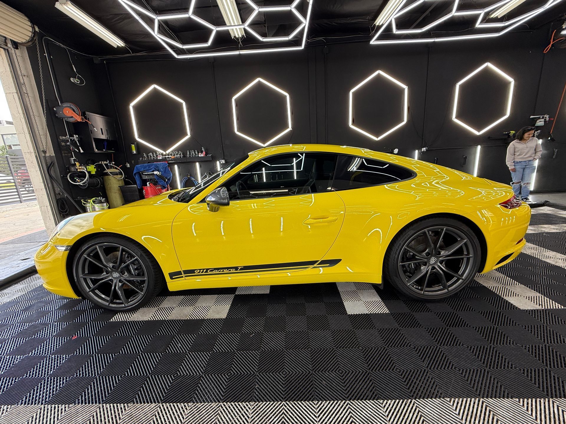 Yellow sports car in a showroom with hexagonal wall lights and patterned black floor.
