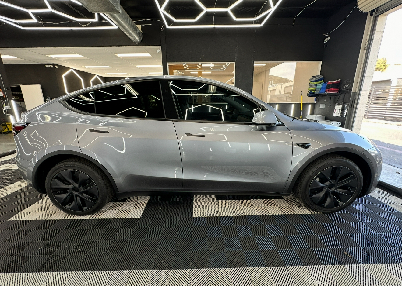 Silver Tesla SUV displayed indoors on patterned flooring under hexagonal ceiling lights