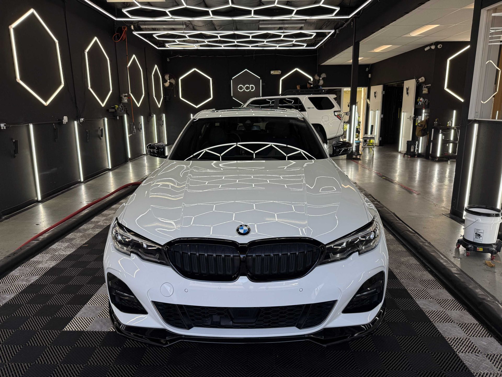 White BMW sedan in a black-lit car wash bay with hexagonal LED lights overhead